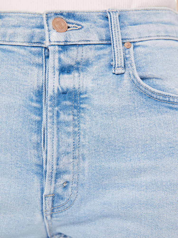 A close up detail swatch of a light blue wash jean featuring light gold hardware and tonal stitching.