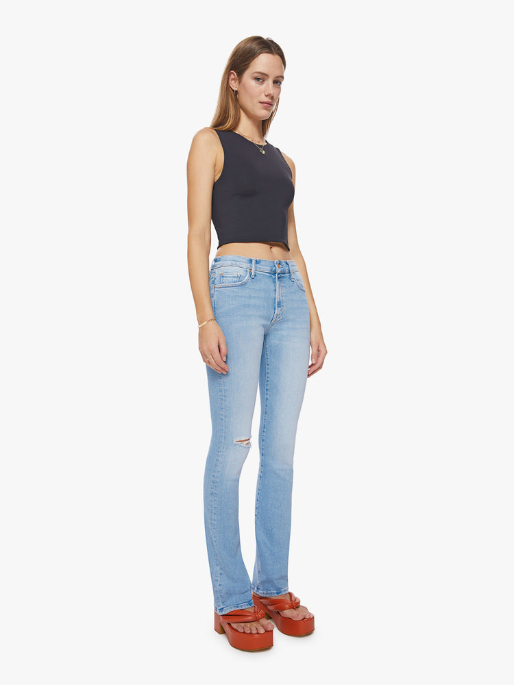Front 3/4 view of a woman mid-rise jeans with a narrow straight leg and a long 34-inch inseam with a clean hem in a light blue with distressed details and a tear knee.