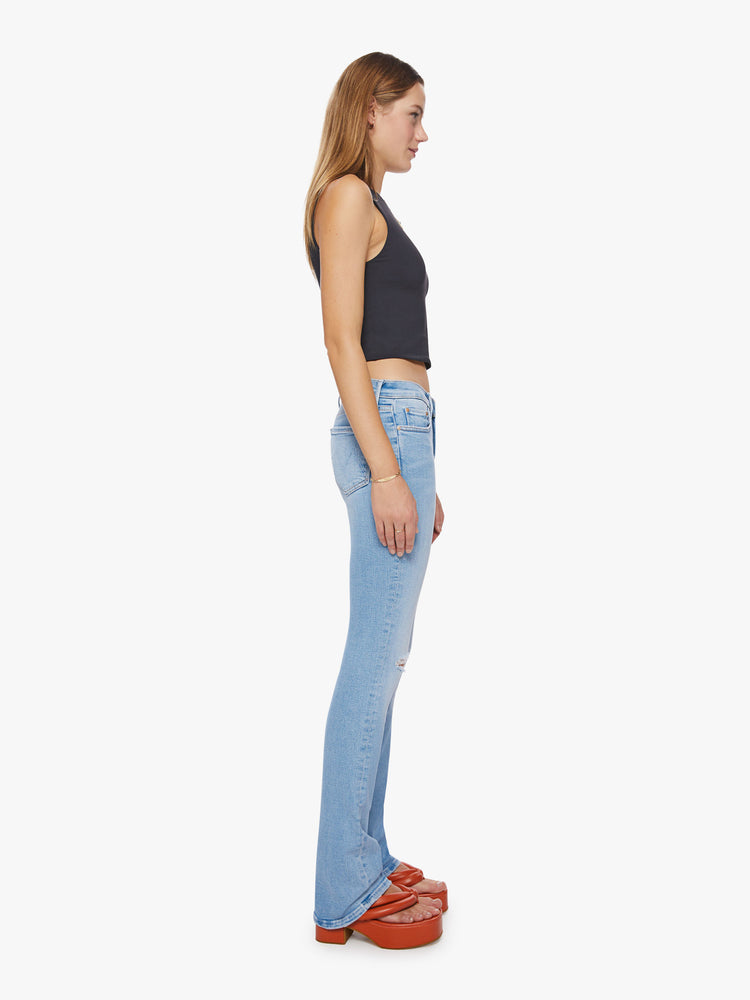 Side view of a woman mid-rise jeans with a narrow straight leg and a long 34-inch inseam with a clean hem in a light blue with distressed details and a tear knee.
