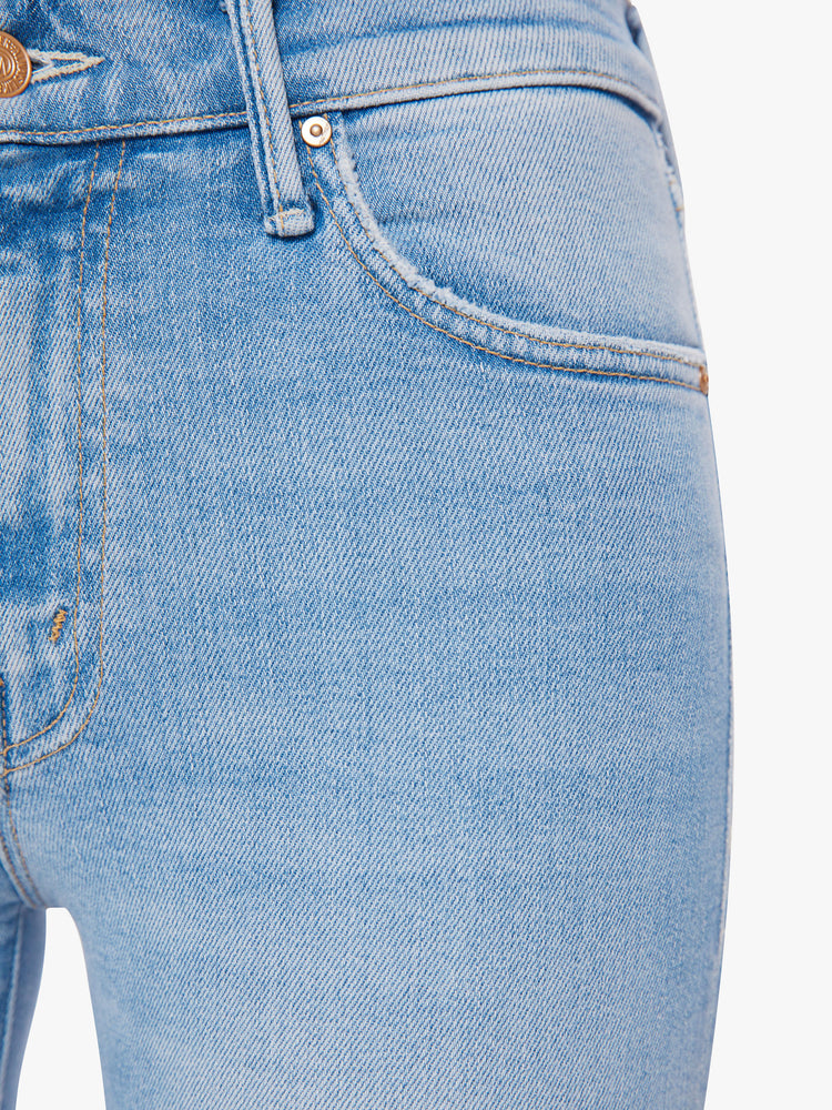 Front close up view of a woman mid-rise jeans with a narrow straight leg and a long 34-inch inseam with a clean hem in a light blue with distressed details and a tear knee.