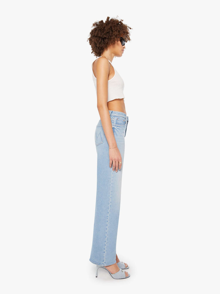 Side view of a woman in light blue super high-rise jeans with a loose fit, wide leg, zip fly and 32-inch inseam with a clean hem. 
