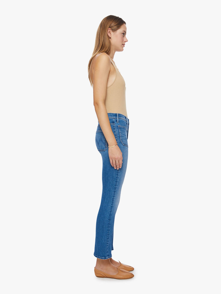 Side view of a woman high-rise bootcut with front patch pockets, an ankle-length inseam and a clean hem in a mid-blue wash.