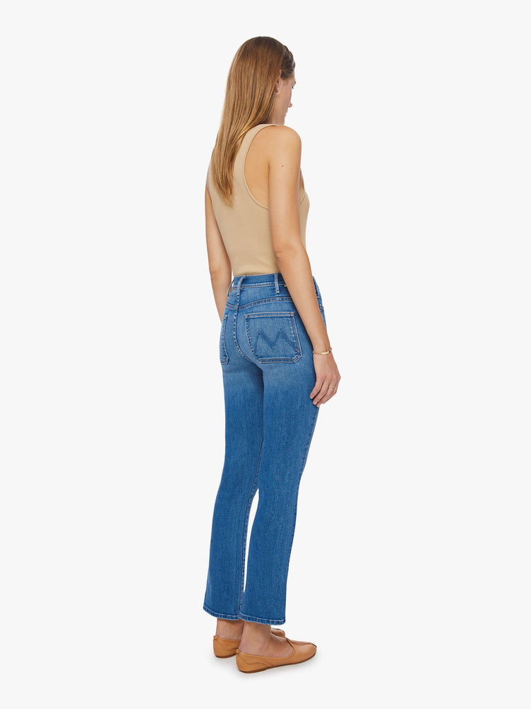 Back view of a woman high-rise bootcut with front patch pockets, an ankle-length inseam and a clean hem in a mid-blue wash.
