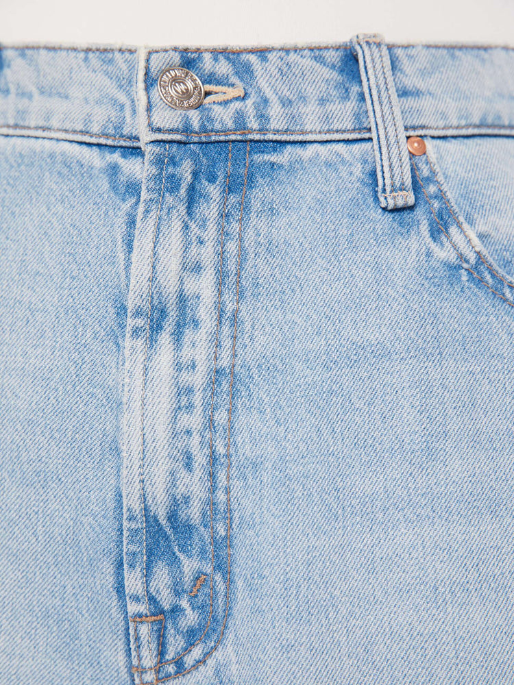 A close up swatch detail view of a light blue wash jean featuring silver and copper hardware and contrast brown thread.