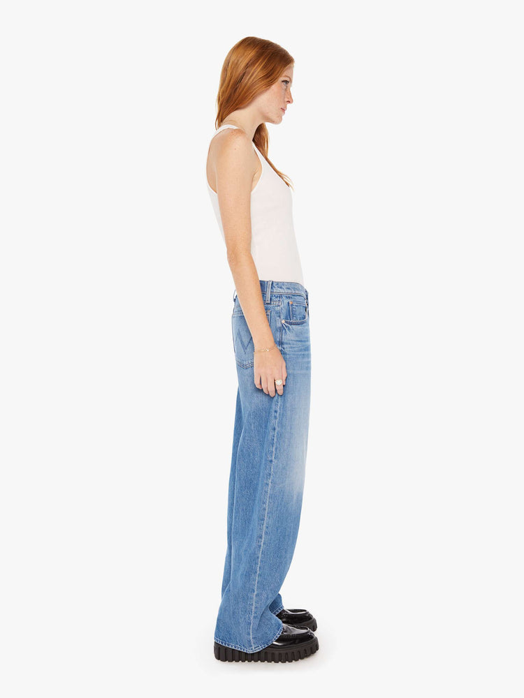 Side view of woman in a mid blue low-rise jeans with a loose wide leg and a long 32-inch inseam with a clean hem.