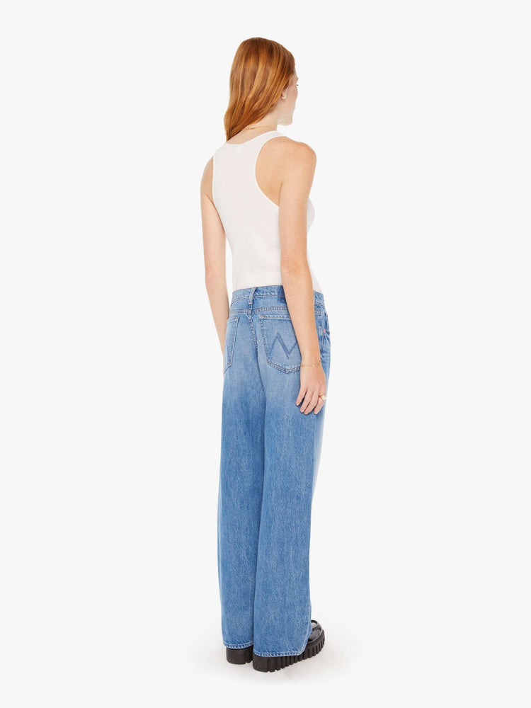 Back view of woman in a mid blue low-rise jeans with a loose wide leg and a long 32-inch inseam with a clean hem.