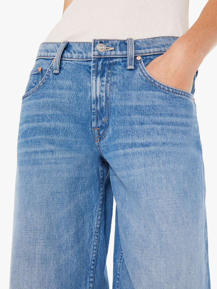 Waist close up view of woman in a mid blue low-rise jeans with a loose wide leg and a long 32-inch inseam with a clean hem.