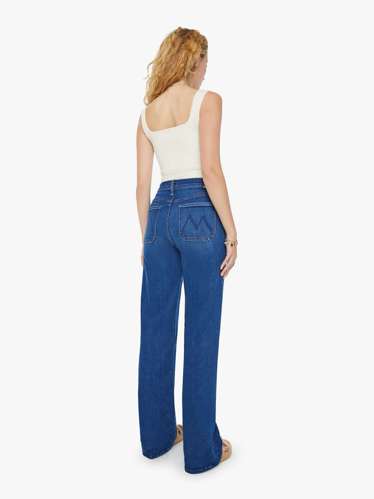 Back view of a woman in dark blue super high-waisted jeans with a loose wide leg, utility-inspired patch pockets, and subltle whiskering and fading at the knee. Styled with a white tank top.