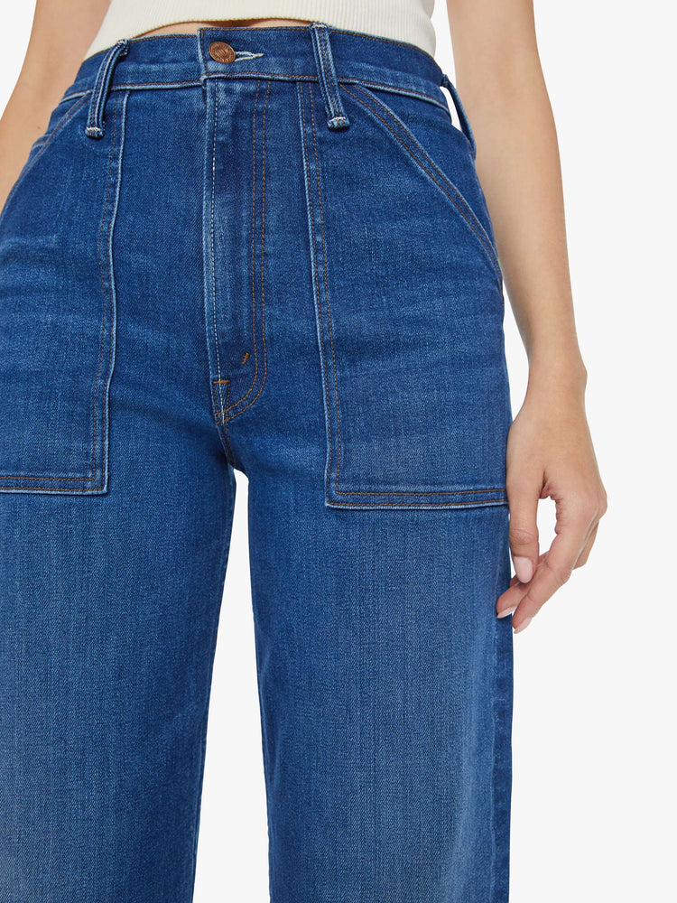 Swatch view of a woman in dark blue super high-waisted jeans with a loose wide leg, utility-inspired patch pockets, and subltle whiskering and fading at the knee. Styled with a white tank top.