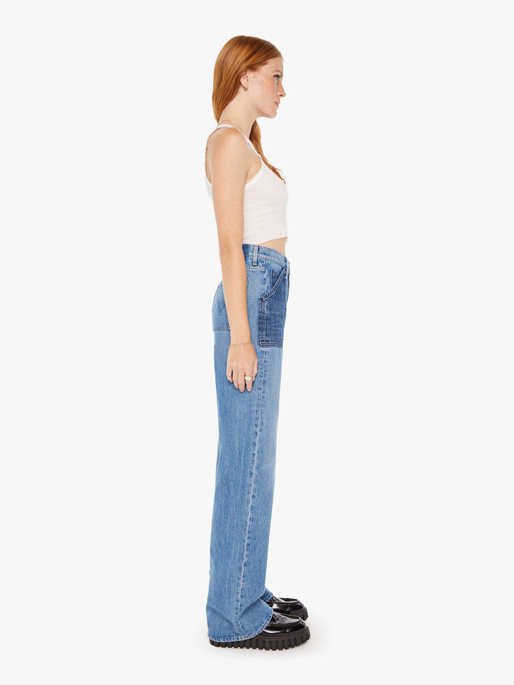 Side view of a woman super high-waisted jeans with a loose fit, wide leg, contrasting patch pockets and 34-inch inseam with a clean hem in a mid blue wash with darker denim pockets.