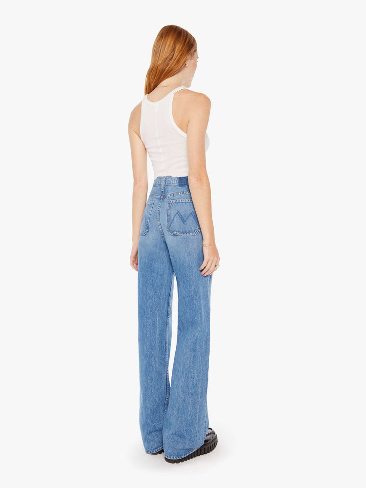 Back view of a woman super high-waisted jeans with a loose fit, wide leg, contrasting patch pockets and 34-inch inseam with a clean hem in a mid blue wash with darker denim pockets.