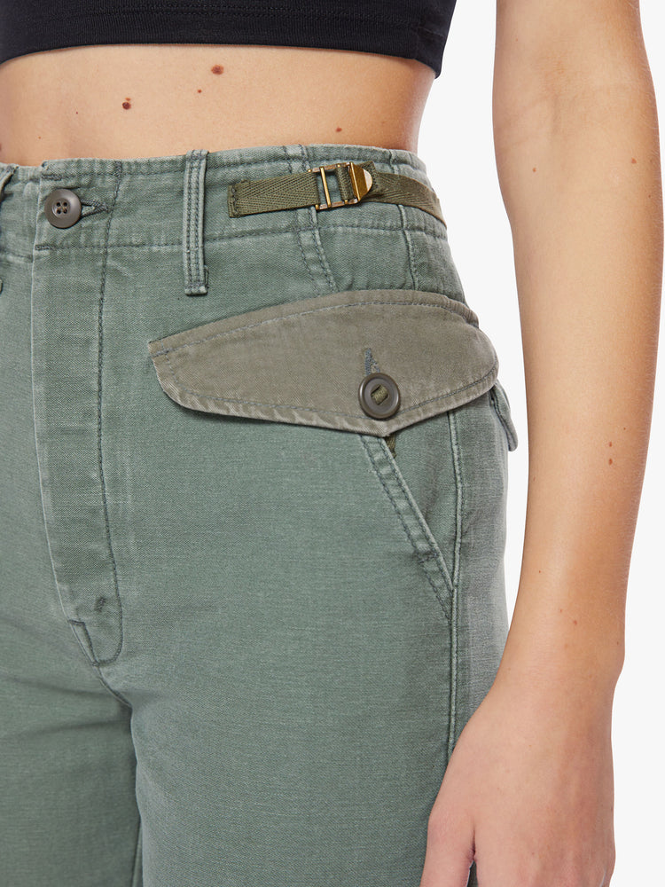 Waist close view of a woman army-green hue cargo pants with a super high rise, patch pockets, a 30-inch inseam and buttons on the hem.