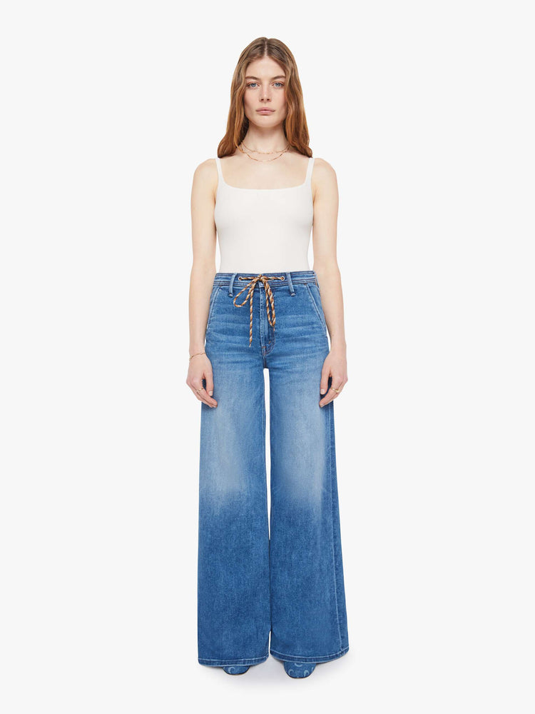 Front view of a woman in a mid-blue wide leg jeans with a high rise, zip fly, colorful drawstring waistband and a long 32-inch inseam with a clean hem.