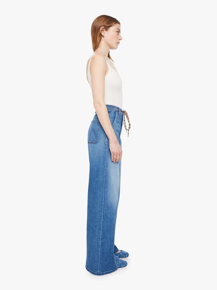 Side view of a woman in a mid-blue wide leg jeans with a high rise, zip fly, colorful drawstring waistband and a long 32-inch inseam with a clean hem.