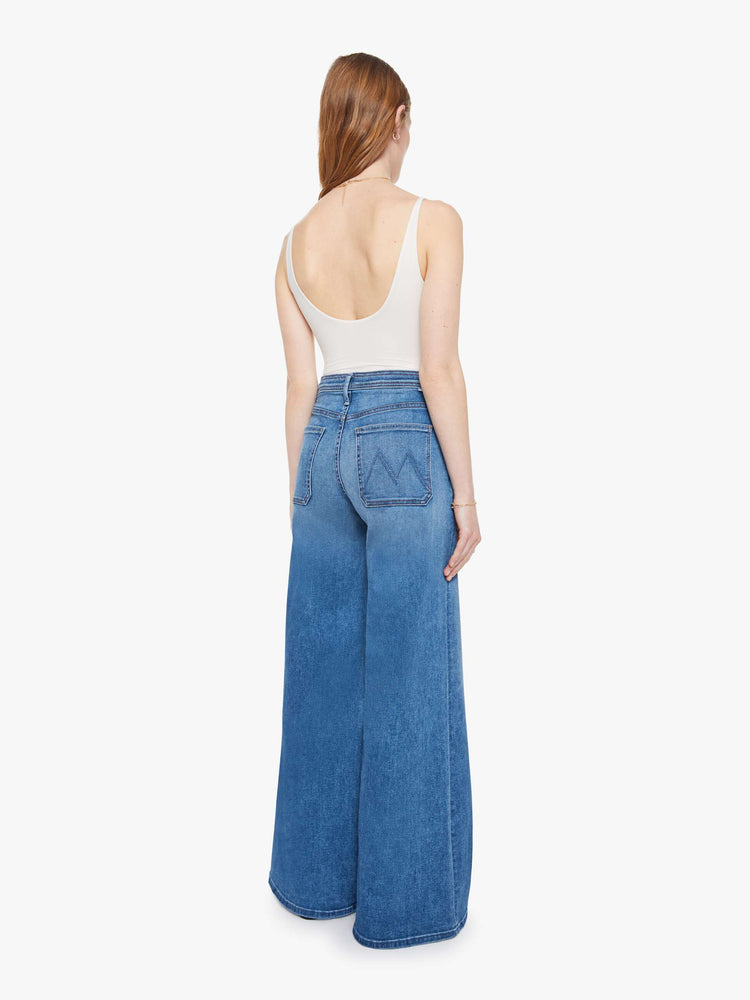 Back view of a woman in a mid-blue wide leg jeans with a high rise, zip fly, colorful drawstring waistband and a long 32-inch inseam with a clean hem.