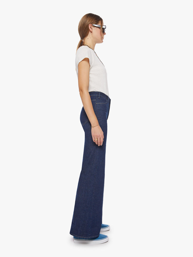 Side view of a woman high-rise jeans with a 34-inch inseam, clean hem and curved patch pockets on the back in a dark blue wash.