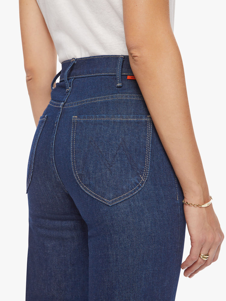 Close up view of a woman high-rise jeans with a 34-inch inseam, clean hem and curved patch pockets on the back in a dark blue wash.