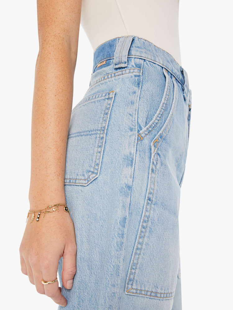 Side close up view of a womens light blue denim featuring a high rise, a wide straight leg, and front patch pockets.