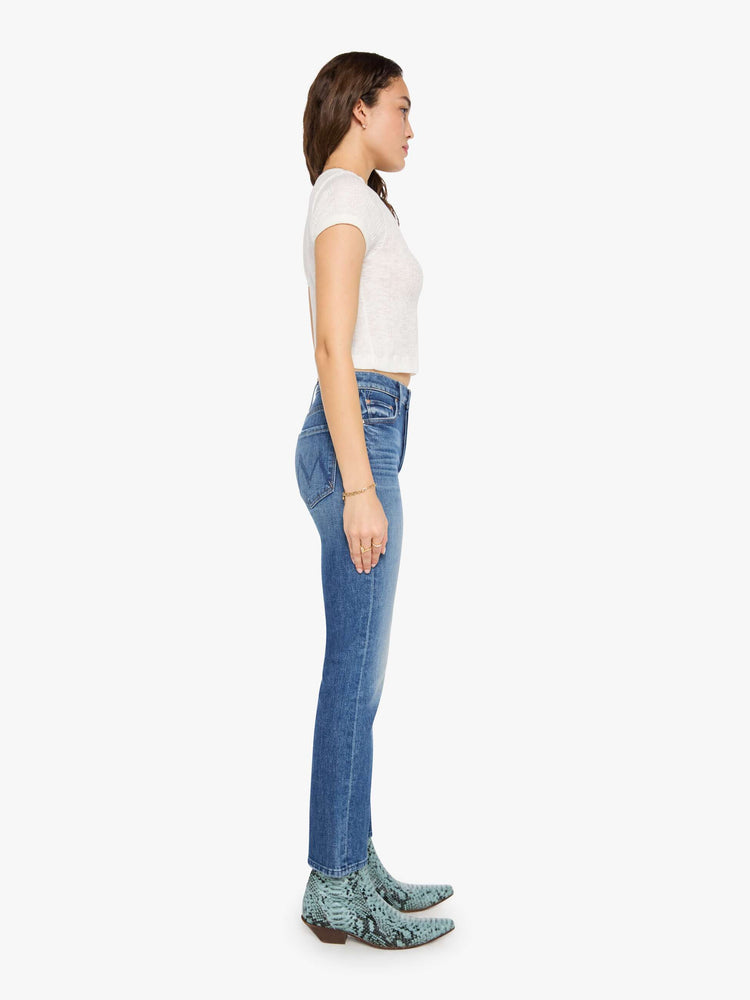 Side view of a woman in med blue high-waisted straight-leg jeans with a button fly, 29-inch inseam and a clean hem.