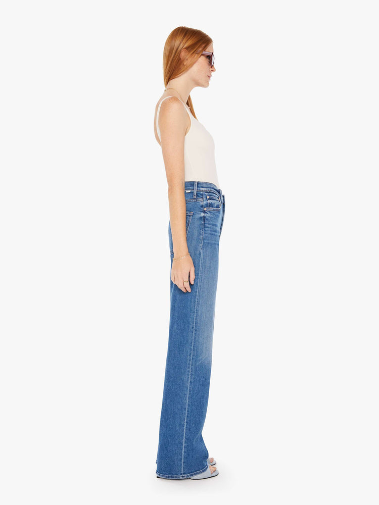 Side view of a womens medium blue wash jean featuring a super high rise and a wide full length leg.