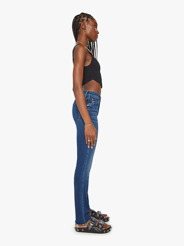 Side view of a woman high-rise straight leg with a 31-inch inseam and a frayed hem in a dark blue wash.