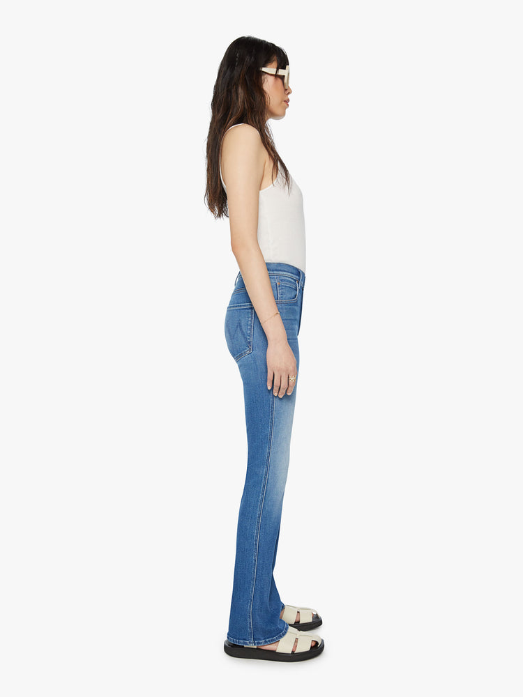 Side view of a woman high-rise flare with a long 34-inch inseam and a clean hem in a mid blue wash.