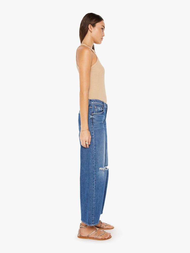 Side view of a womens medium blue wash jean featuring a relaxed low rise, a wide leg, with distressed details at the knees.