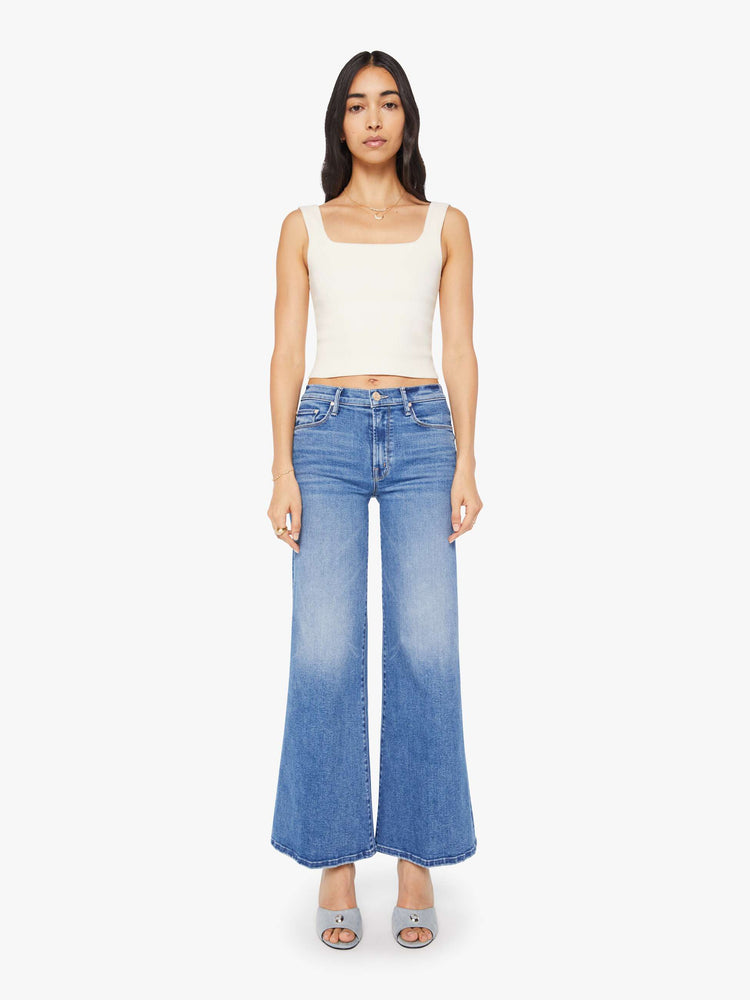 Front view of a woman in a mid blue high-rise pants with a flared, wide leg and 31-inch inseam with a clean hem.