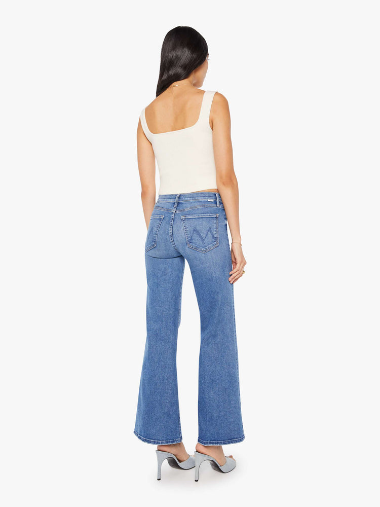 Back view of a woman in a mid blue high-rise pants with a flared, wide leg and 31-inch inseam with a clean hem.
