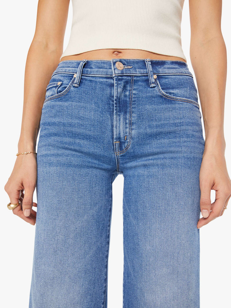 Close up view of a woman in a mid blue high-rise pants with a flared, wide leg and 31-inch inseam with a clean hem.