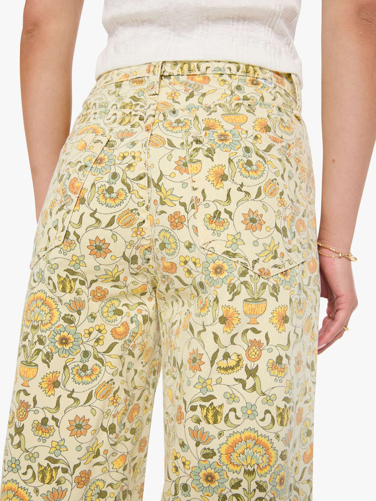 Back view of a woman in a pale yellow fresh florals  wide legs pant with a high rise with a slightly dropped crotch, zip fly, low-set back pockets and a 32-inch inseam with a clean hem.