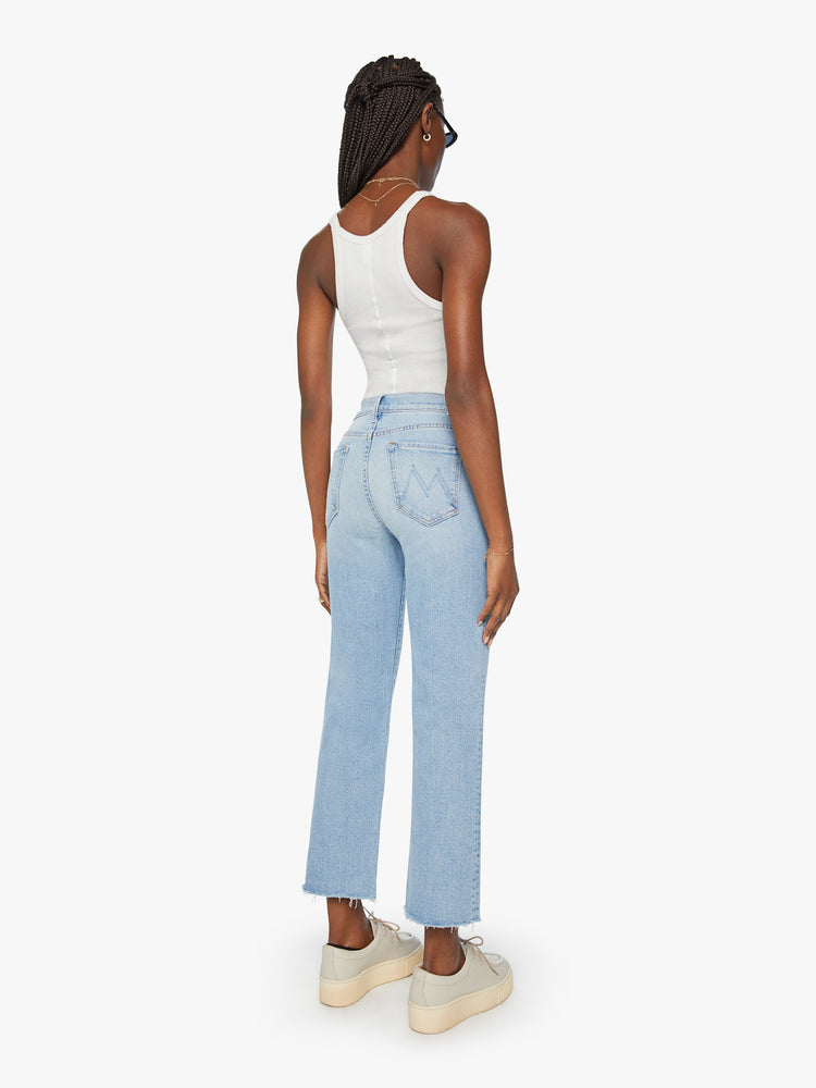 Back view of woman high-rise, straight-leg with an ankle-length inseam and a frayed hem in a light blue wash.