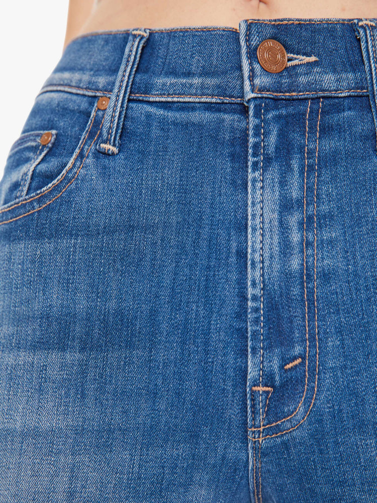 A close up detail swatch view of a medium blue wash jean featuring copper hardware and contrast brown thread.