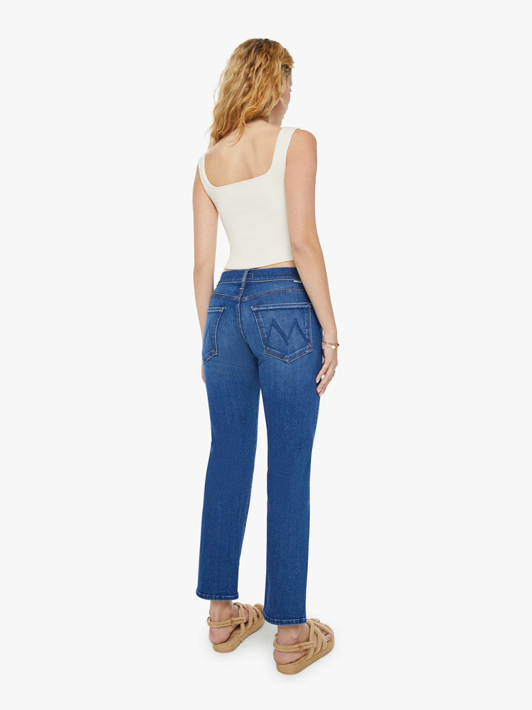 Back view of a woman in a dark blue straight-leg jean with super-subtle whiskering and fading at the knee. Styled with a white tank top.