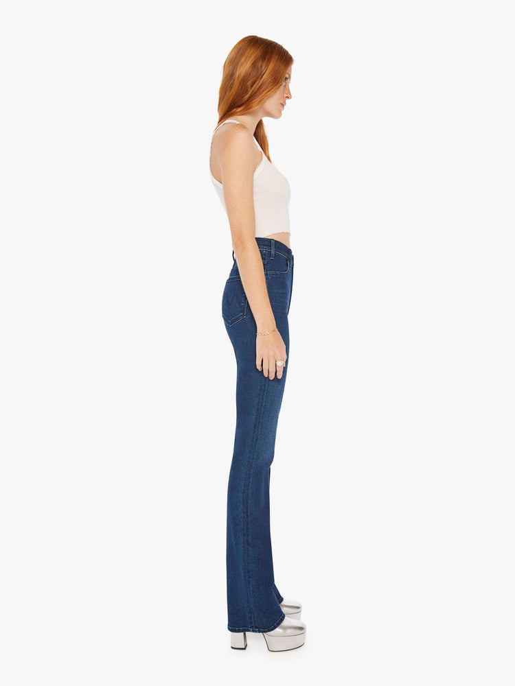Side view of a woman dark blue wash high-waisted flare jeans with a long 34-inch inseam and a clean hem.