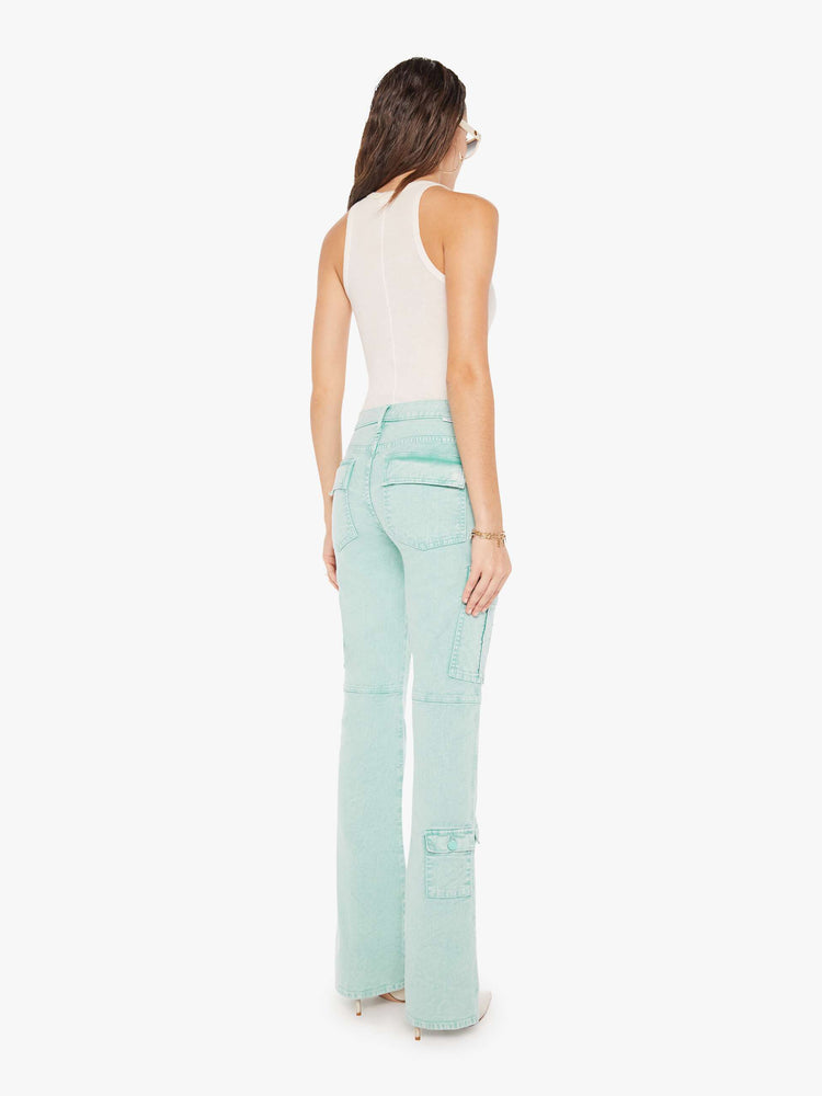 Back view of a woman wearing a light teal wash jean featuring darker teal hues around the seams, a high rise, a full length flare, and cargo pockets, paired with a white tank top.