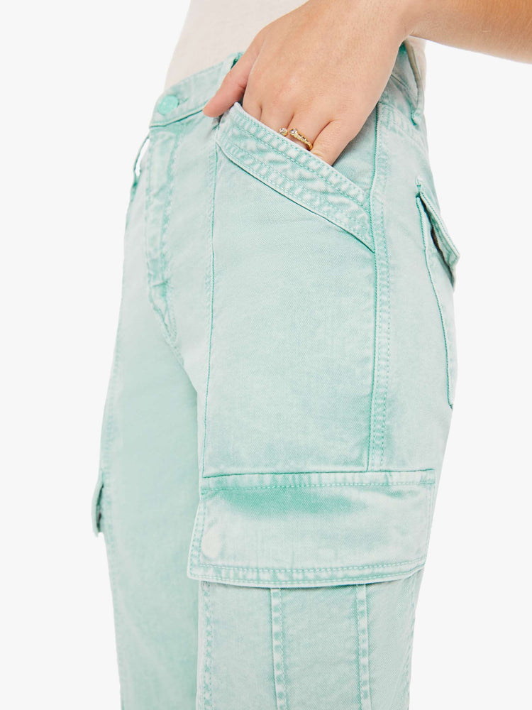 Side close up view of a woman wearing a light teal wash jean featuring darker teal hues around the seams, a high rise and cargo pockets.