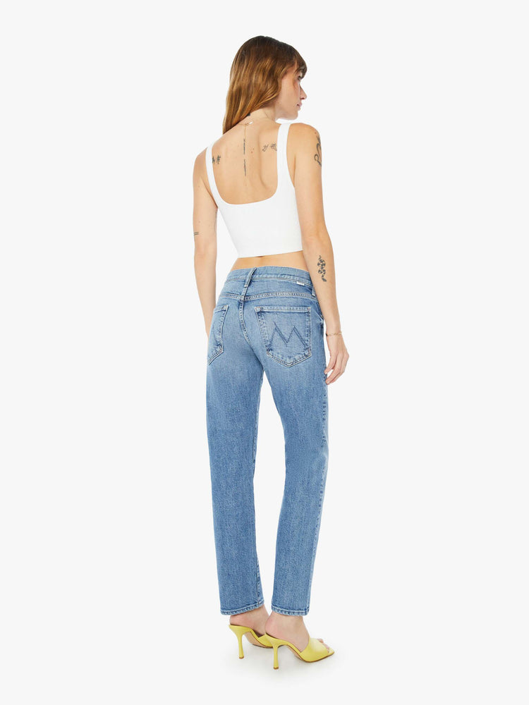 A back view of a woman wearing a medium blue wash jean featuring a mid rise and a relaxed straight leg, paired with a cropped white tank top.