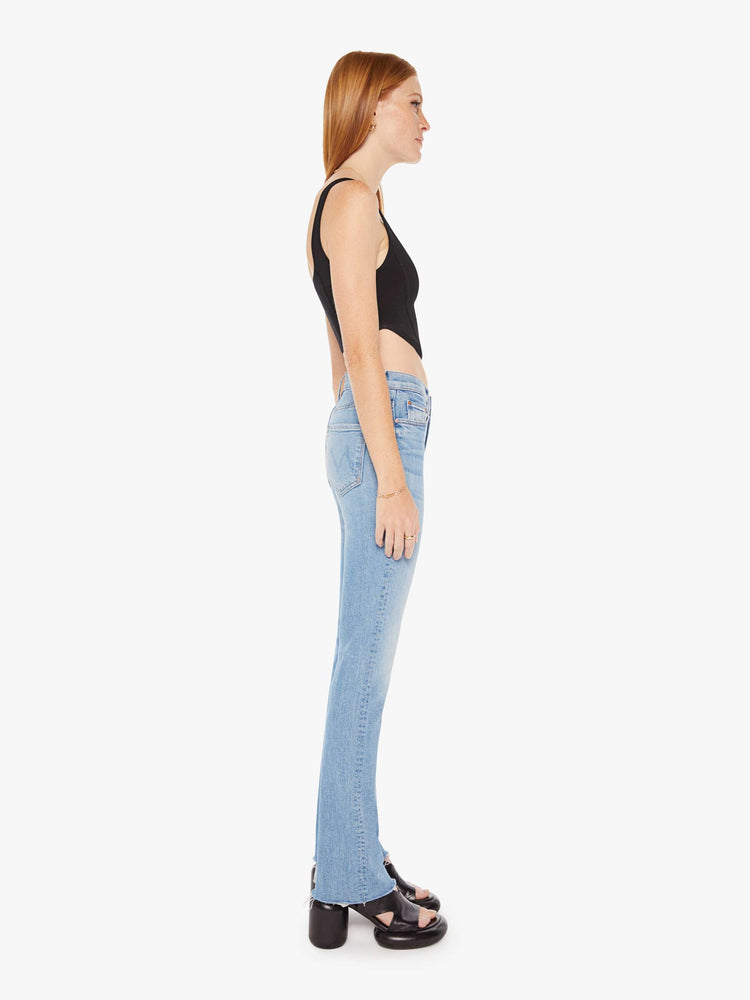 Side view of a womens light blue jean featuring a high rise and a frayed bootcut.