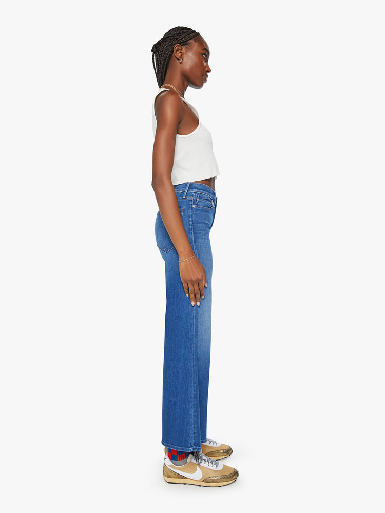 Side view of a woman mid blue flared, wide-leg jean with a high rise and a clean, ankle-length inseam.