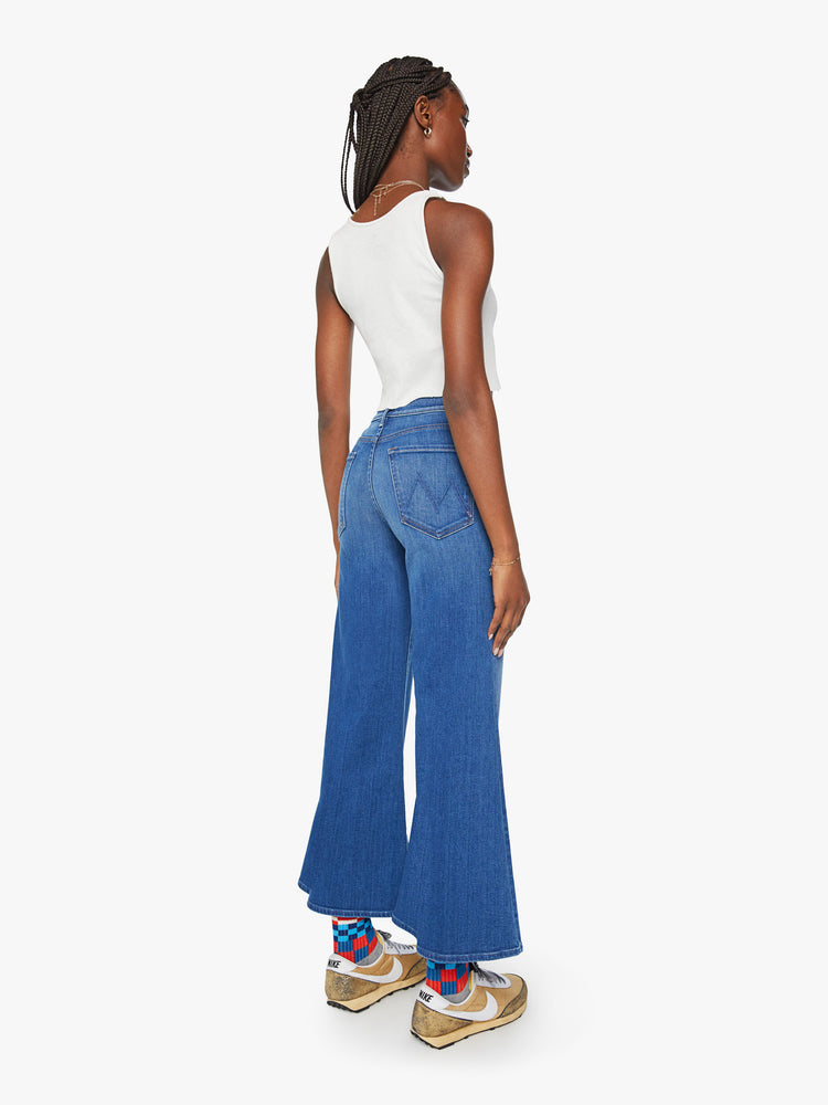 Back view of a woman mid blue flared, wide-leg jean with a high rise and a clean, ankle-length inseam.