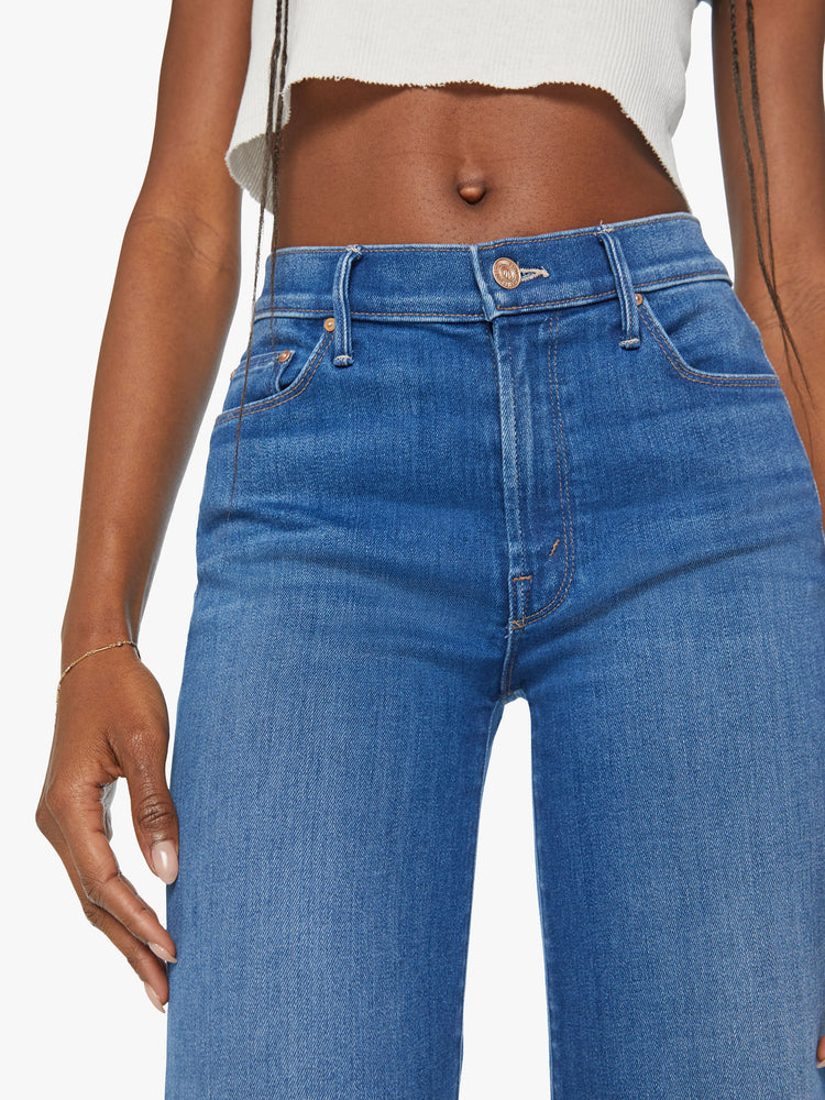 Waist close up view of a woman mid blue flared, wide-leg jean with a high rise and a clean, ankle-length inseam.