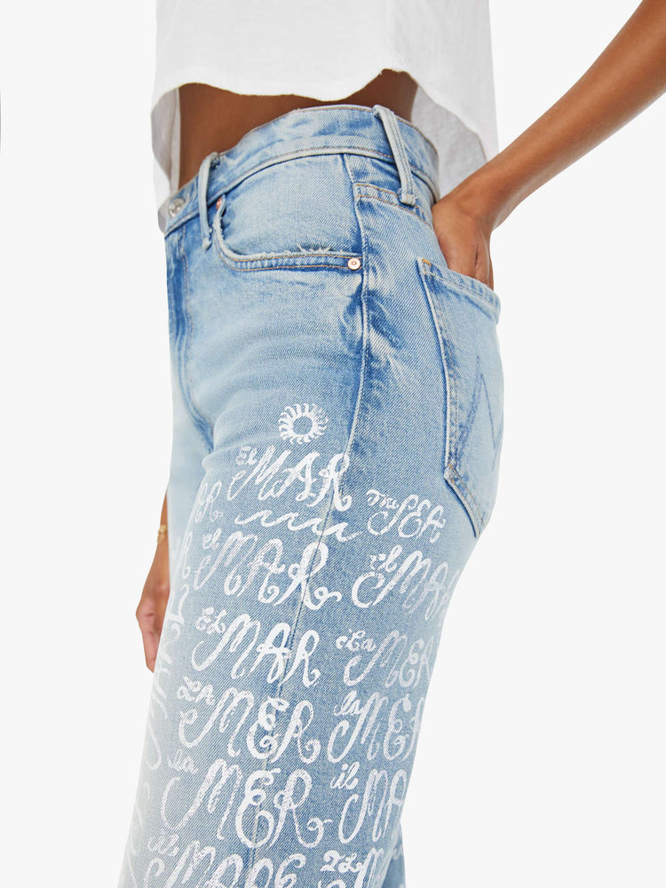 Swatch view of a woman in light blue high-waisted straight leg jeans with whiskering, fading and screen printed text in different languages on the legs.