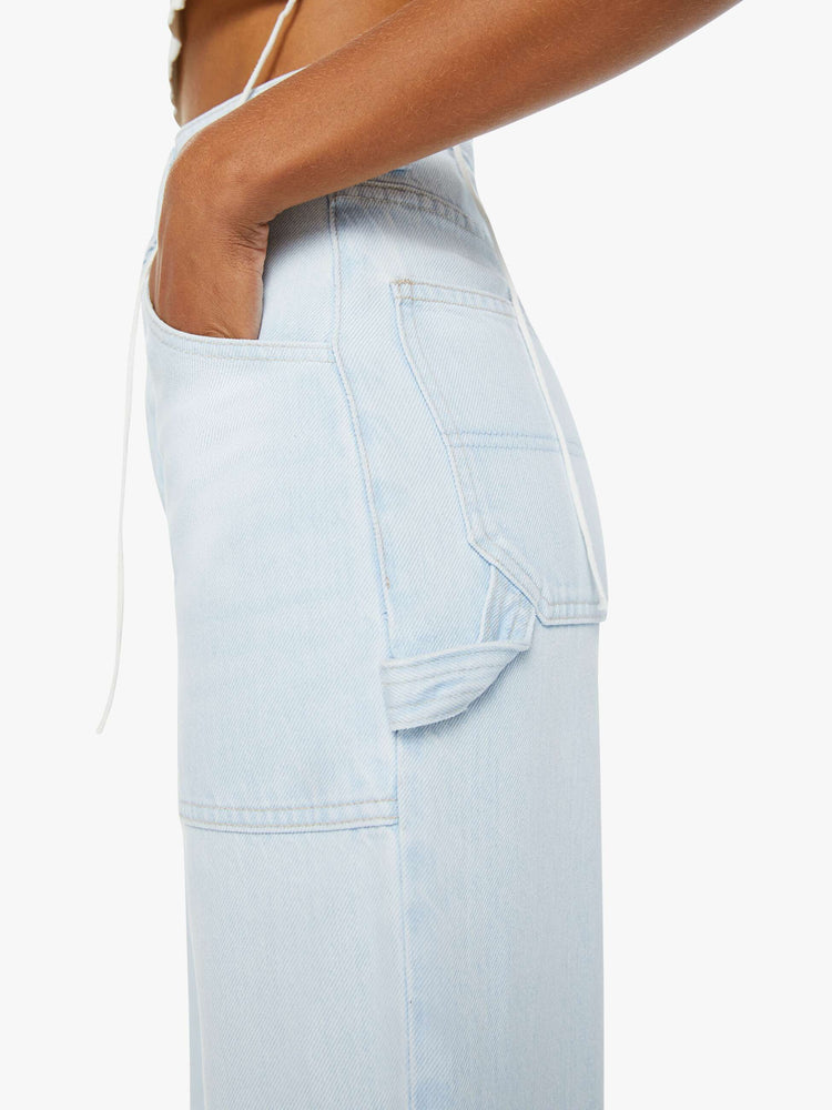 Detailed side view of a woman in light blue super high-rise jeans, designed with a button-fly, workwear-inspired patch pockets, a hammer loop, ankle-length inseam and slouchy fit with a pretzel-detailed button.