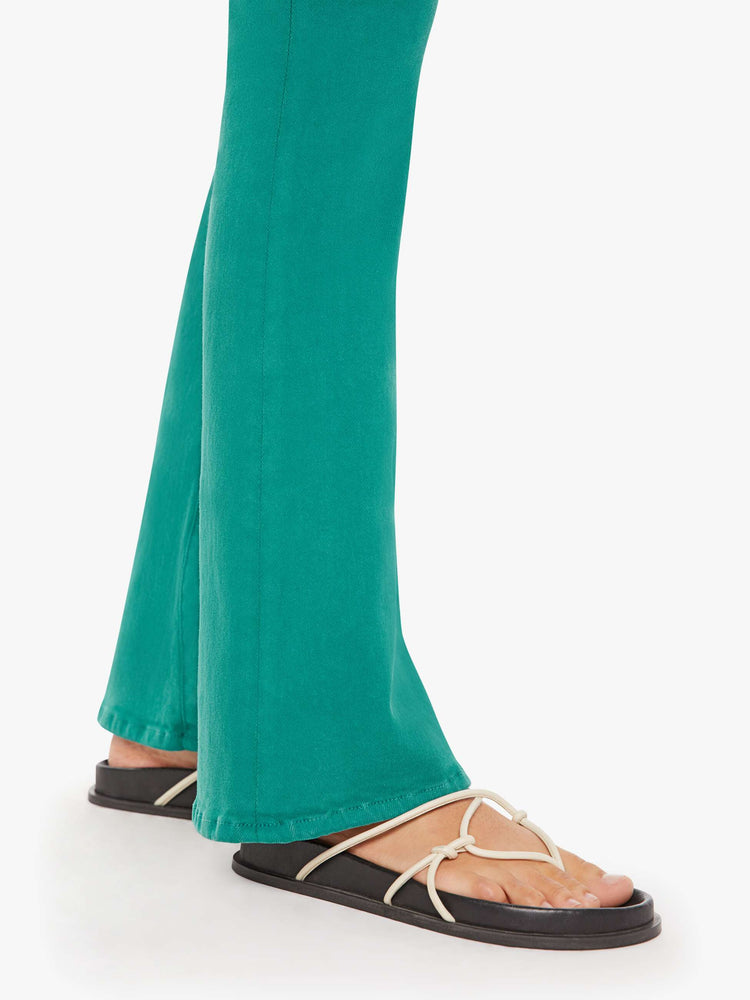 Side close up view of a womens teal pant featuring a mid rise and long flare leg.