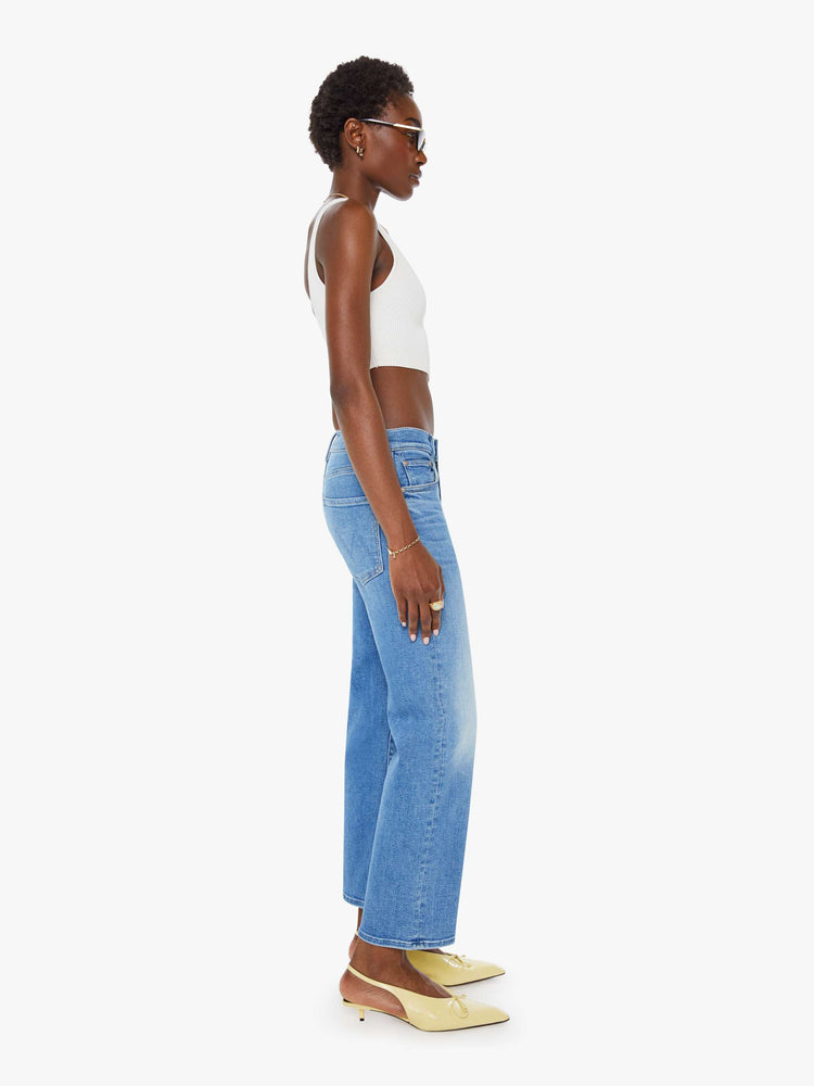 Side view of a woman mid blue wash mid-rise jeans with a wide straight leg, zip fly and clean ankle-length inseam.