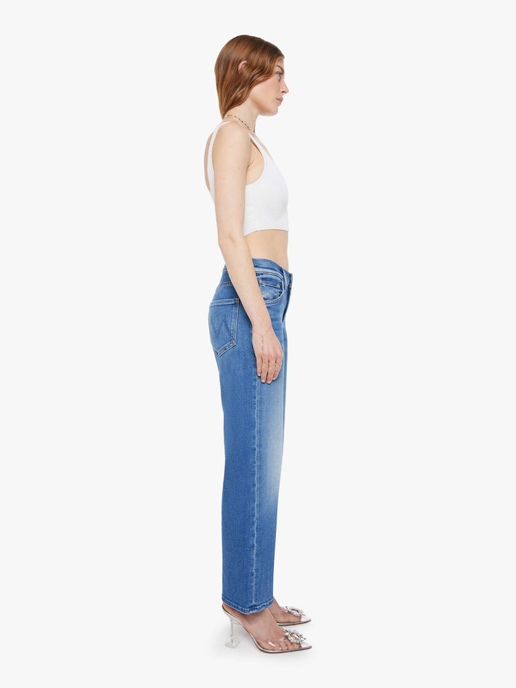 Side view of woman in a mid blue mid-rise jeans with a wide straight leg, zip fly and clean ankle-length inseam.