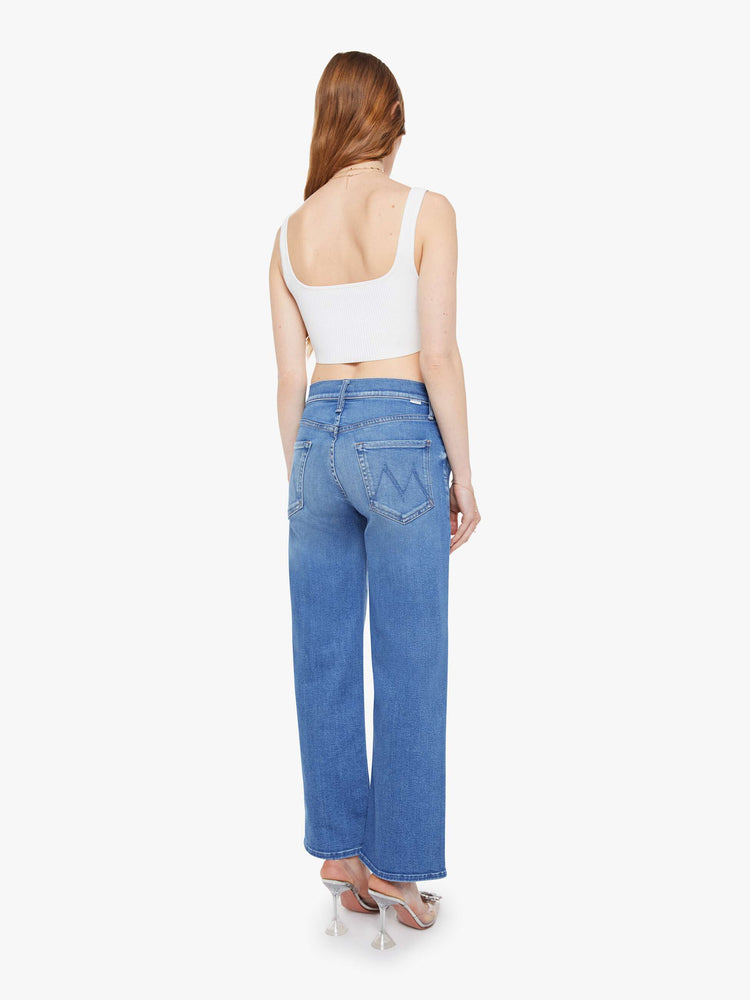 Back view of woman in a mid blue mid-rise jeans with a wide straight leg, zip fly and clean ankle-length inseam.