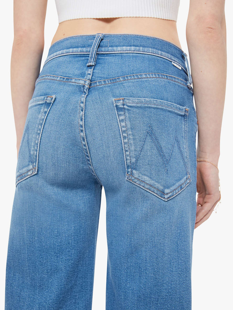 Close up view of woman in a mid blue mid-rise jeans with a wide straight leg, zip fly and clean ankle-length inseam.