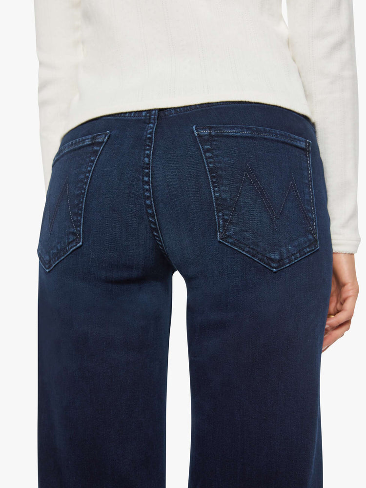 Close up view of a woman in dark denim mid-rise jeans with a wide straight leg, zip fly and clean ankle-length inseam.